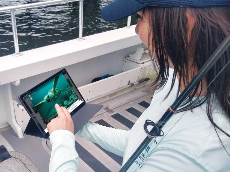 A woman on a boat holding a fishing pole while using the web app on an iPad