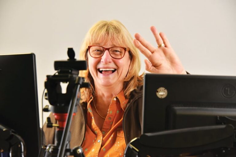 A photo of Christiane Schmullius smiling brightly and waving at the camera from behind some equipment