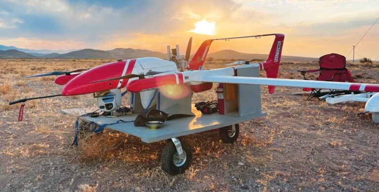 A red and white drone sitting on a carrier in the desert