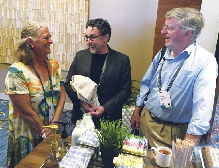 Three people standing around a refreshments table, talking and laughing