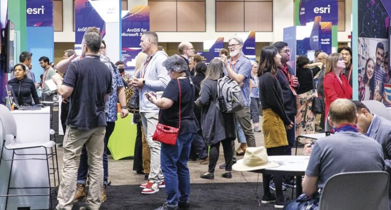 People gathered in the Expo Hall around Esri signage, talking to each other and watching demonstrations