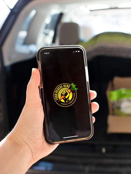A hand holding a smartphone with the Food Rescue Hero app on it