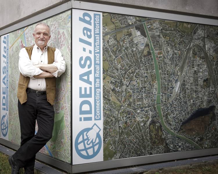 Josef Strobl standing against a sign with a map on it with his arms crossed