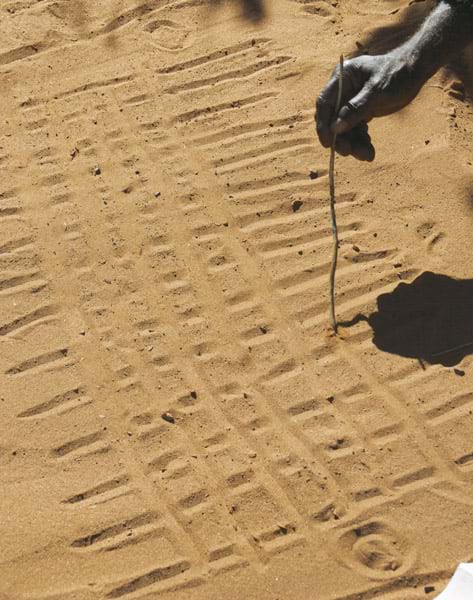 A hand drawing a pattern in the sand with a stick