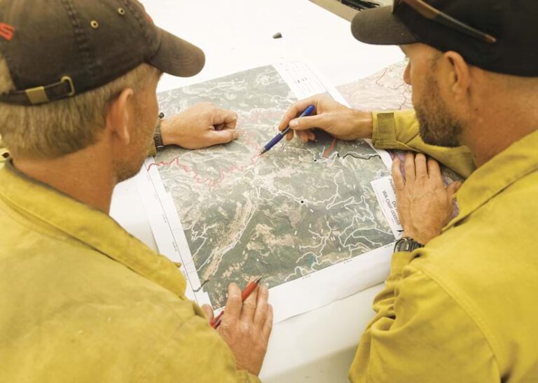Two firefighters looking at a paper map that depicts a wildfire