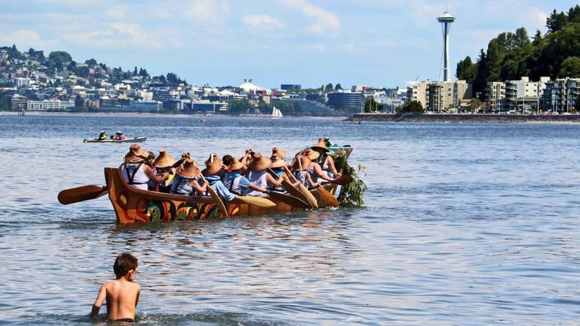A canoe takes to the water at Alki Landing as part of the Intertribal Canoe Journey