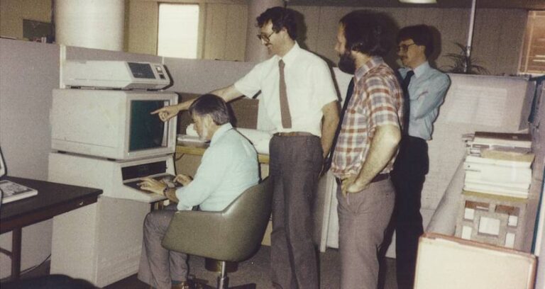 Four men gathered around a large computer in the early 1990s Four men gathered around a large computer in the early 1990s