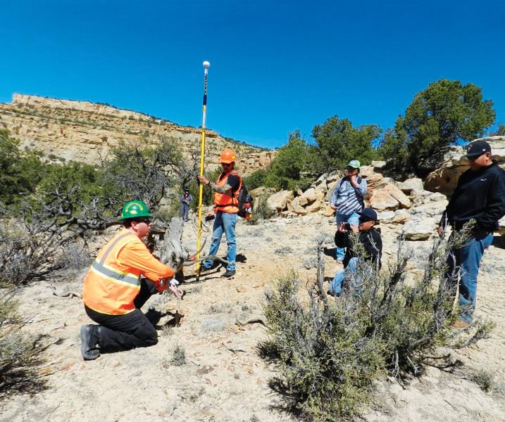 Two individuals conduct fieldwork on a rocky landscape while three others look on