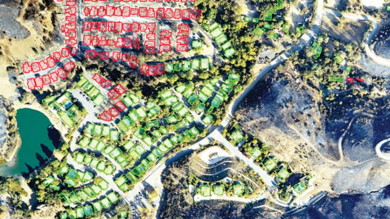 An aerial photo of a residential area with burn scars around it showing red shapes that mark damaged buildings and green shapes that denote undamaged buildings