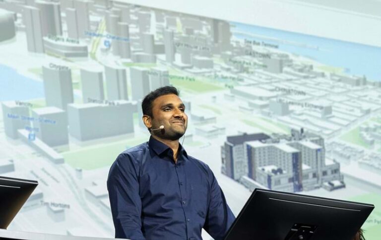 A smiling man standing in front of a big screen with a 3D map on it