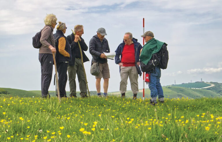 Six individuals gathered in a field on a hill, looking at papers