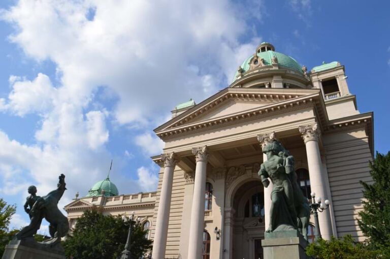 A government building with two domes and two statues in front of it