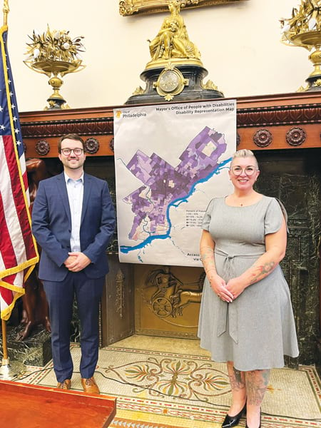 Two people stand in front of an old fireplace and a map entitled “Disability Representation Map.”