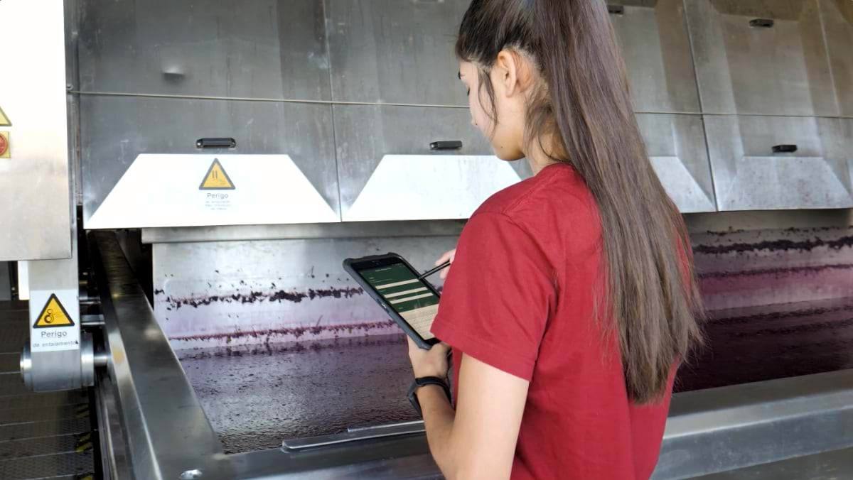 Woman recording data standing next to a vat of grape juice