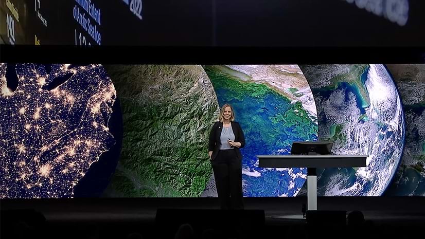 A person standing on stage at an event in front of a large screen with many different views of Earth