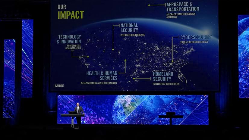 A person standing on a conference stage in front of many large screens