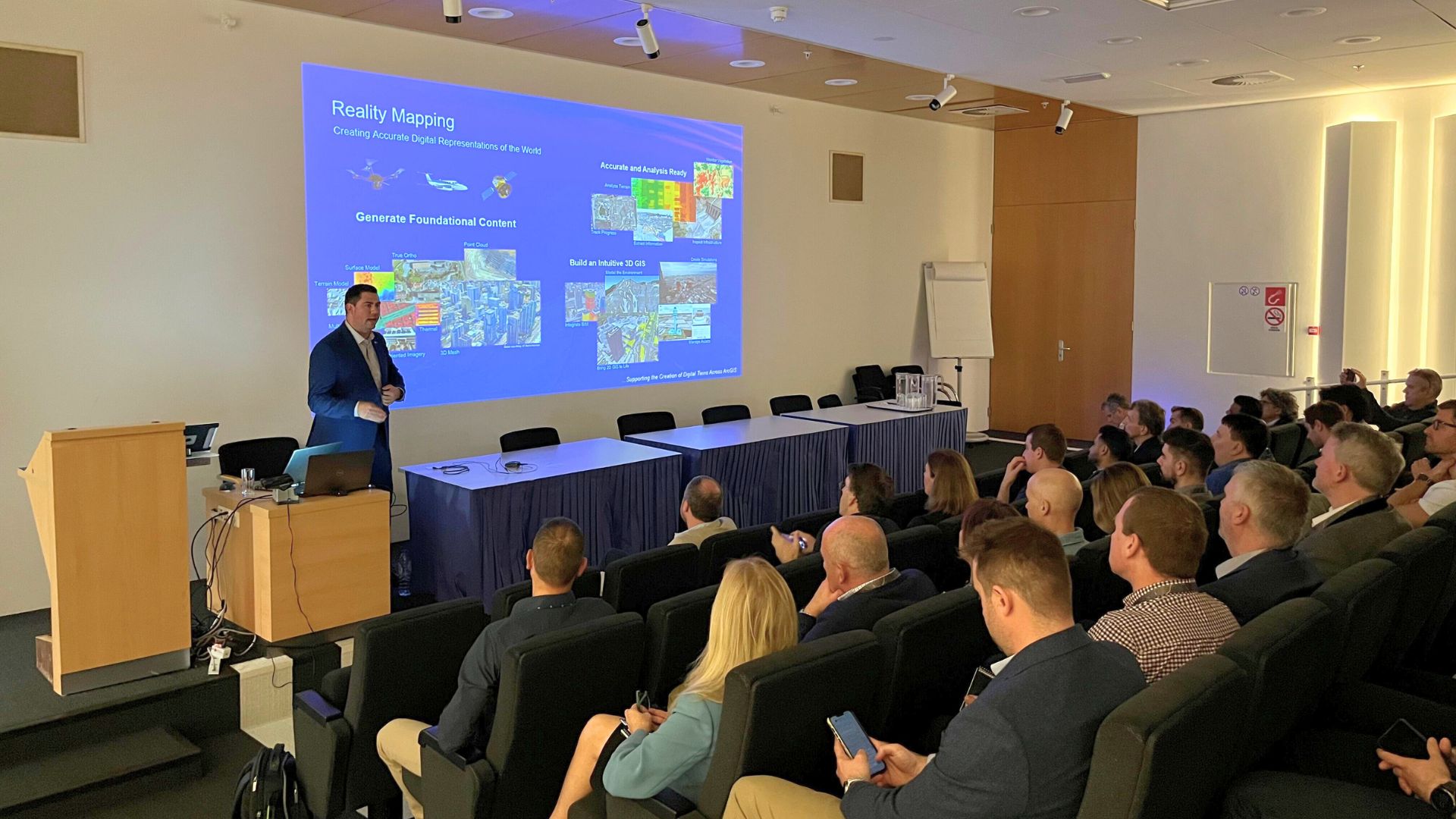 Image of a person presenting to room with a slideshow in the background.