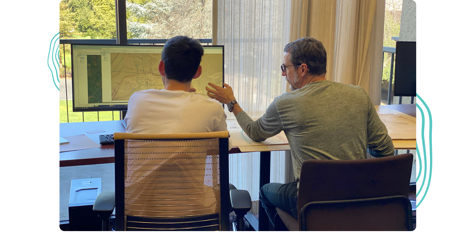 A view from behind of David and a student georefencing historical maps on a desktop computer.