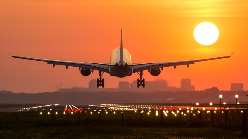 Passenger jet with landing gear extended, descending toward a brightly lit runway at sunset. © 2025 Adobe Stock. All rights reserved.