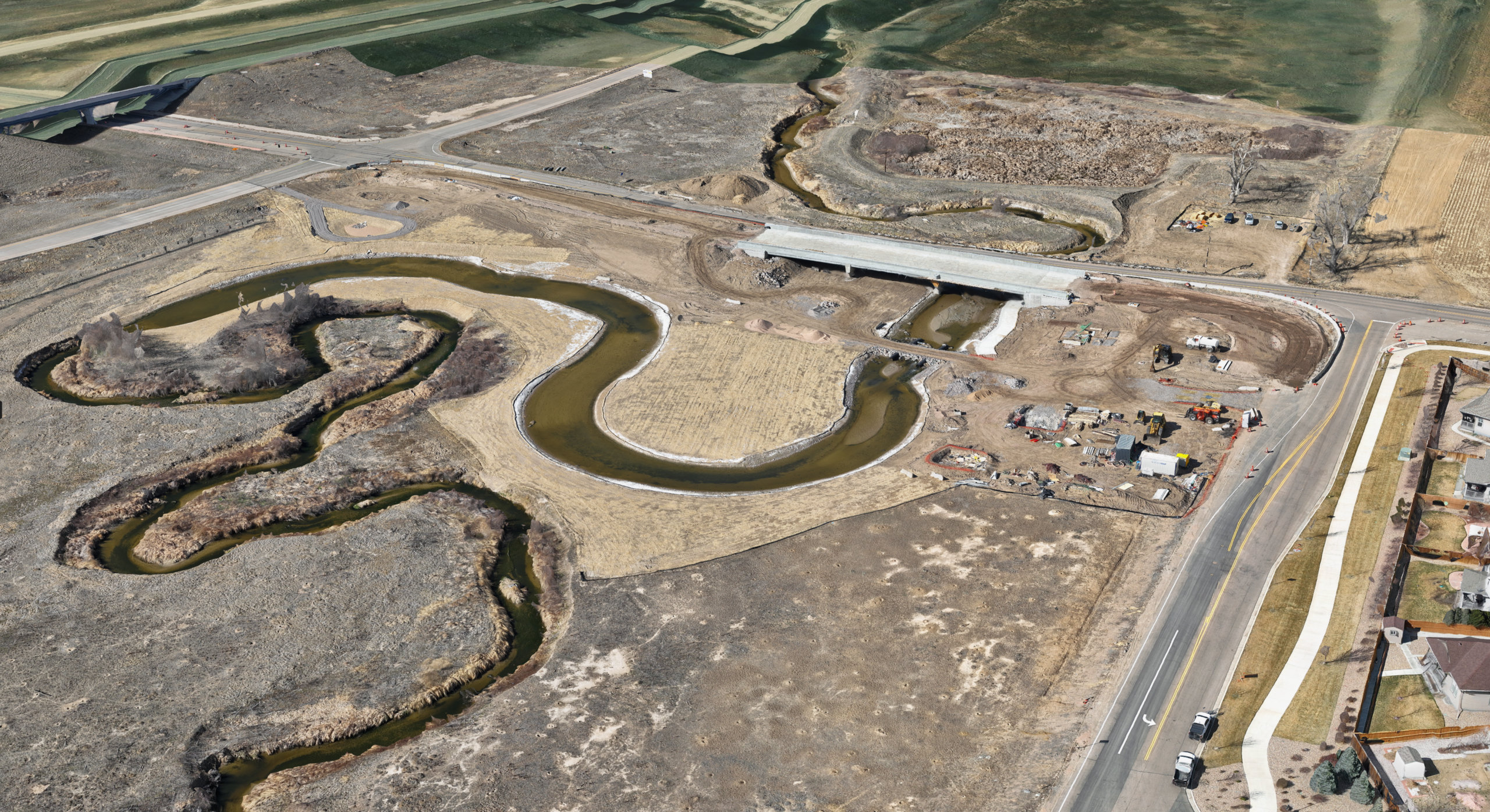 Aerial view of a winding creek flowing through a construction area with a bridge crossing and nearby roadways.