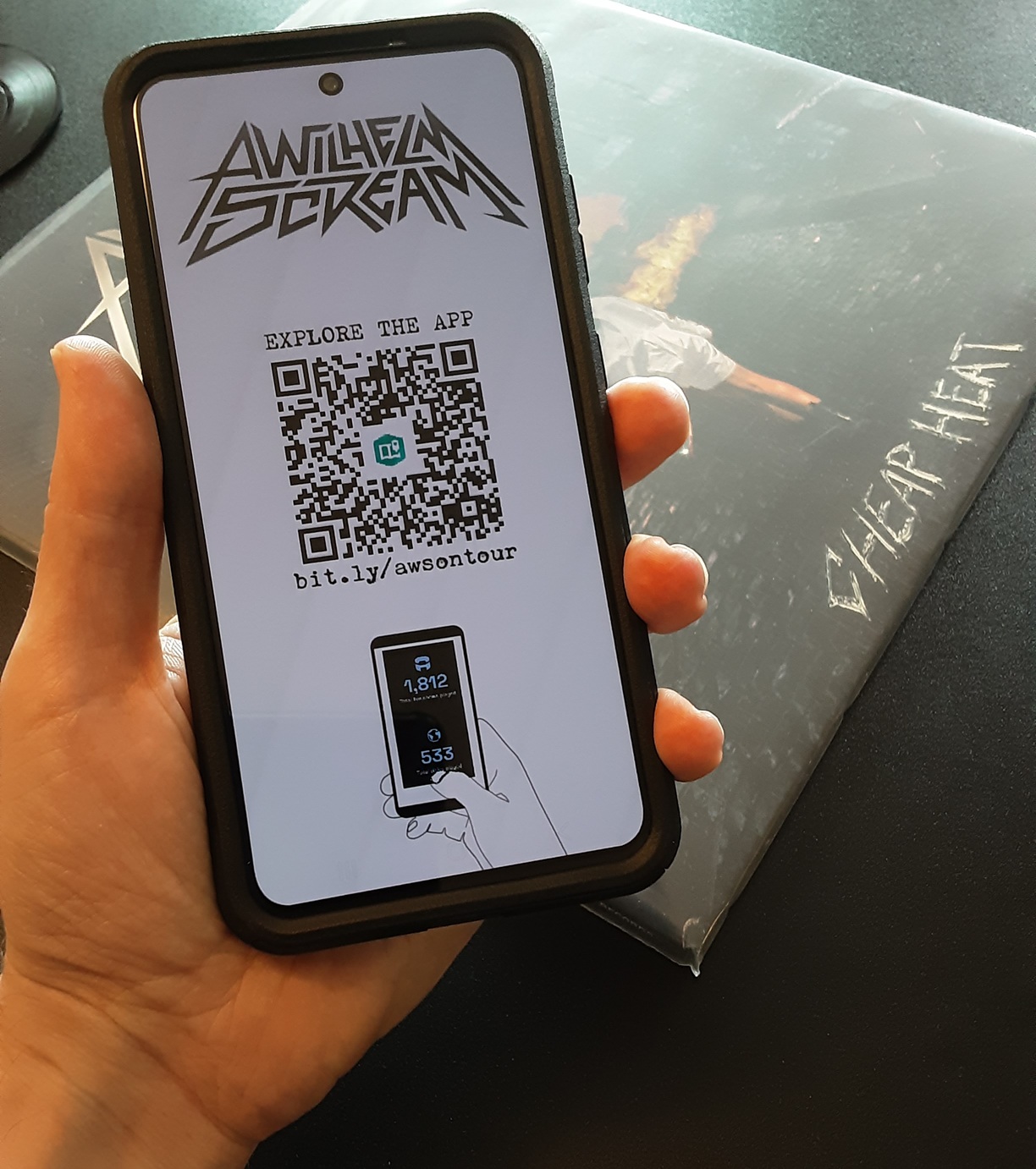 A hand holds a smart phone with a band name and QR code on the screen.