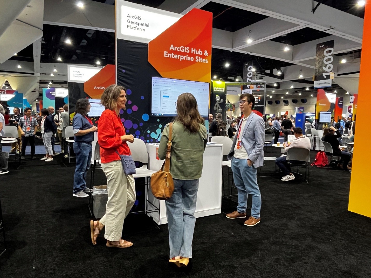 Three people talking and looking at the large monitor at the ArcGIS Hub and Enterprise Sites Esri User Conference kiosk