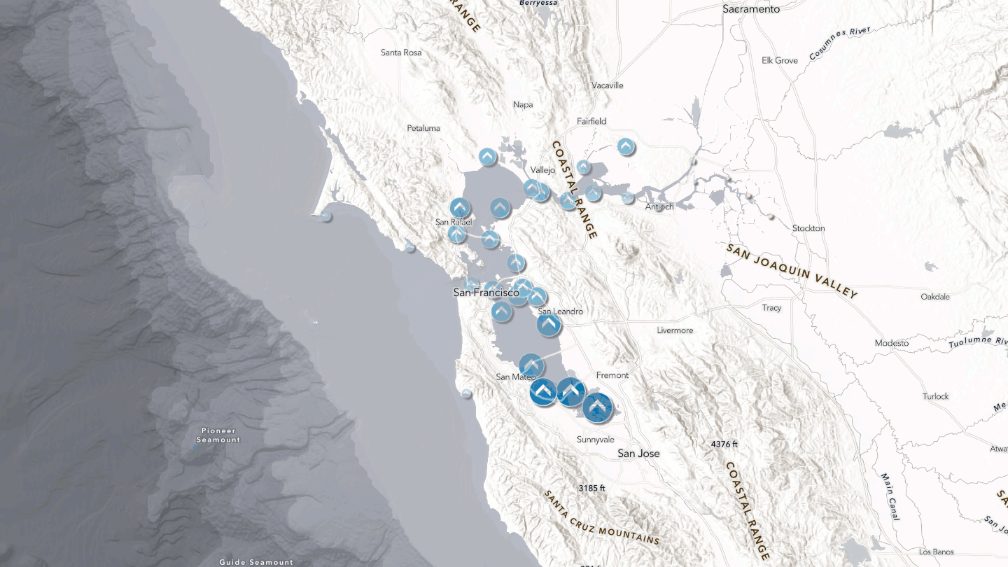 Animated map of the San Francisco Bay region showing predicted tidal water levels at NOAA CO-OPS monitoring stations. Water level stations are represented by blue symbols positioned throughout the bay, from the Pacific coast and Golden Gate through San Francisco Bay and into the Sacramento-San Joaquin Delta. As the animation progresses through a 24-hour period, station symbols change in size and shade to represent rising and falling tidal heights. Larger, darker blue symbols indicate higher water levels, while smaller, lighter symbols indicate lower water levels. The pattern of changing symbols reveals how tidal fluctuations move from the Pacific Ocean through the Golden Gate and propagate across the bay and inland waterways.