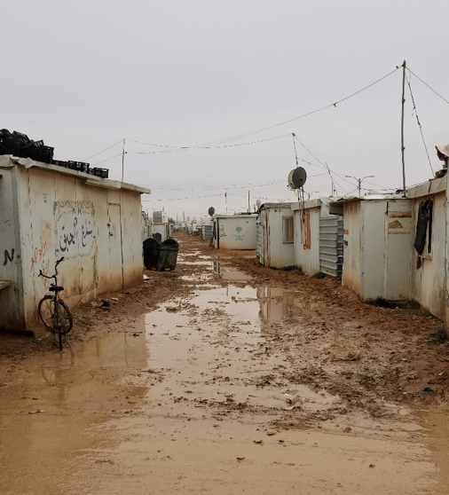 A muddy, shelter-lined road in the refugee camp