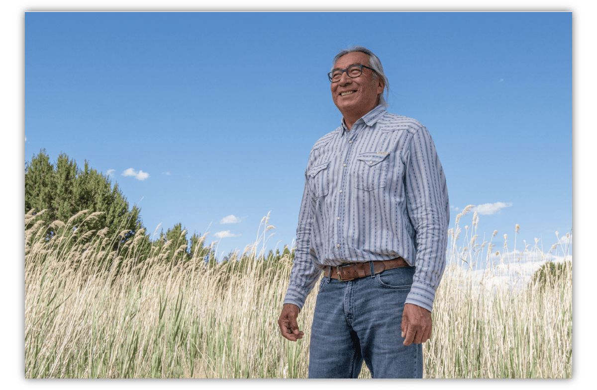 A man is seen from the waist up standing in a grass field on a blue-skied day