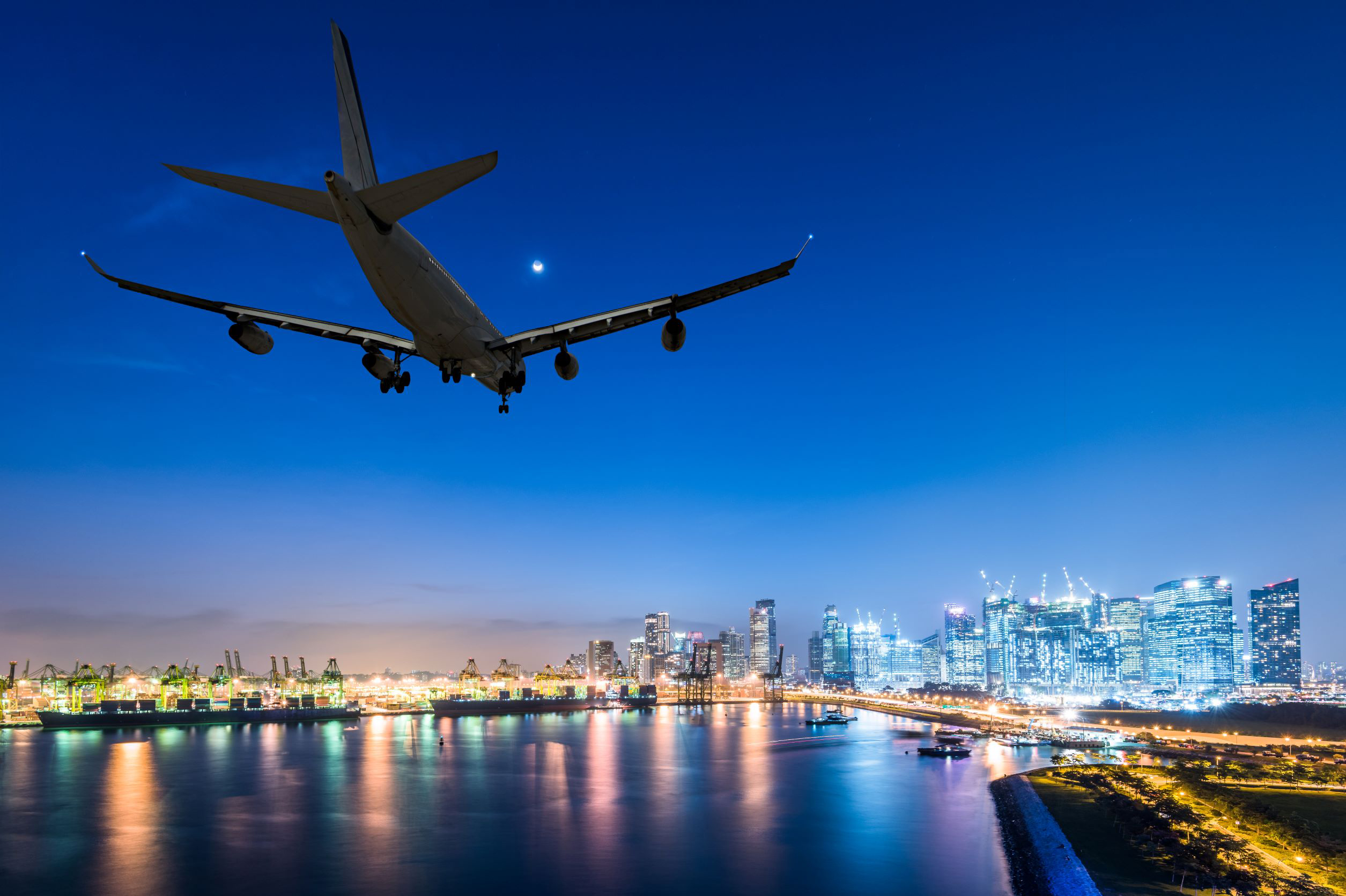 Image of an airplane flying over a city sky at dusk.