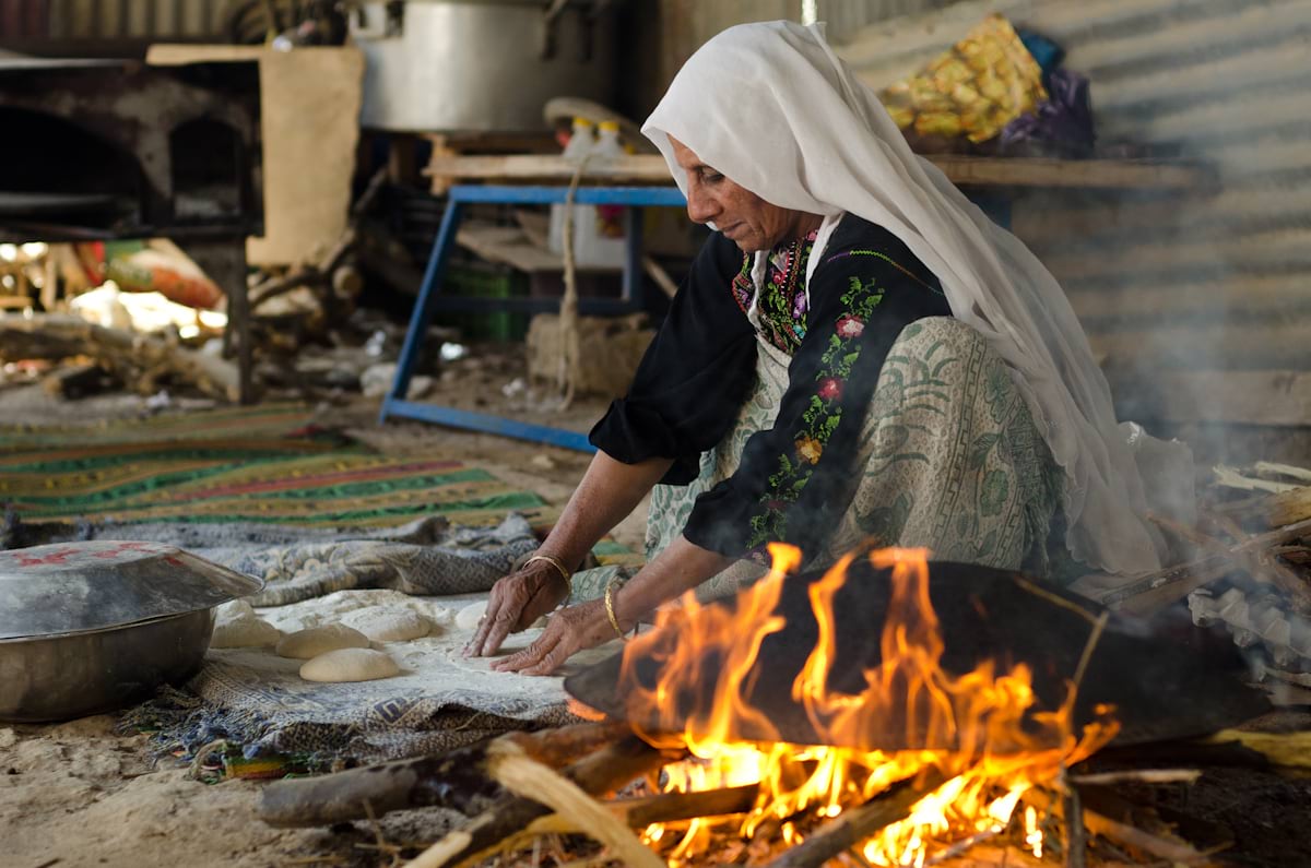 A person rolls bread dough on the ground by an open fire A person rolls bread dough on the ground by an open fire