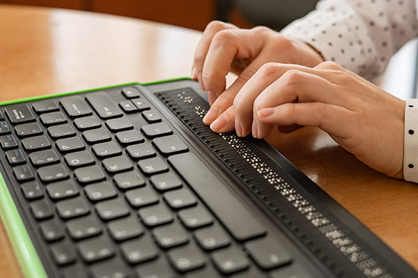 A person using a Braille keyboard types on a computer