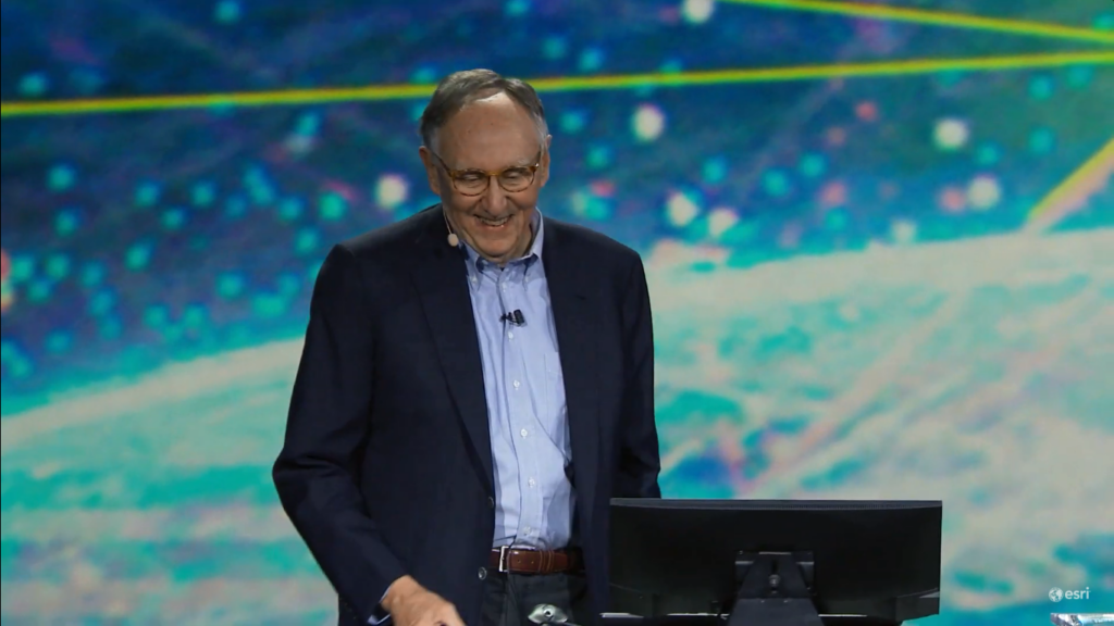 Jack Dangermond at podium smiling with screen behind him.