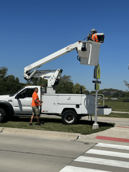 A white utility truck with one street technician standing in front of it and another up in the basket.