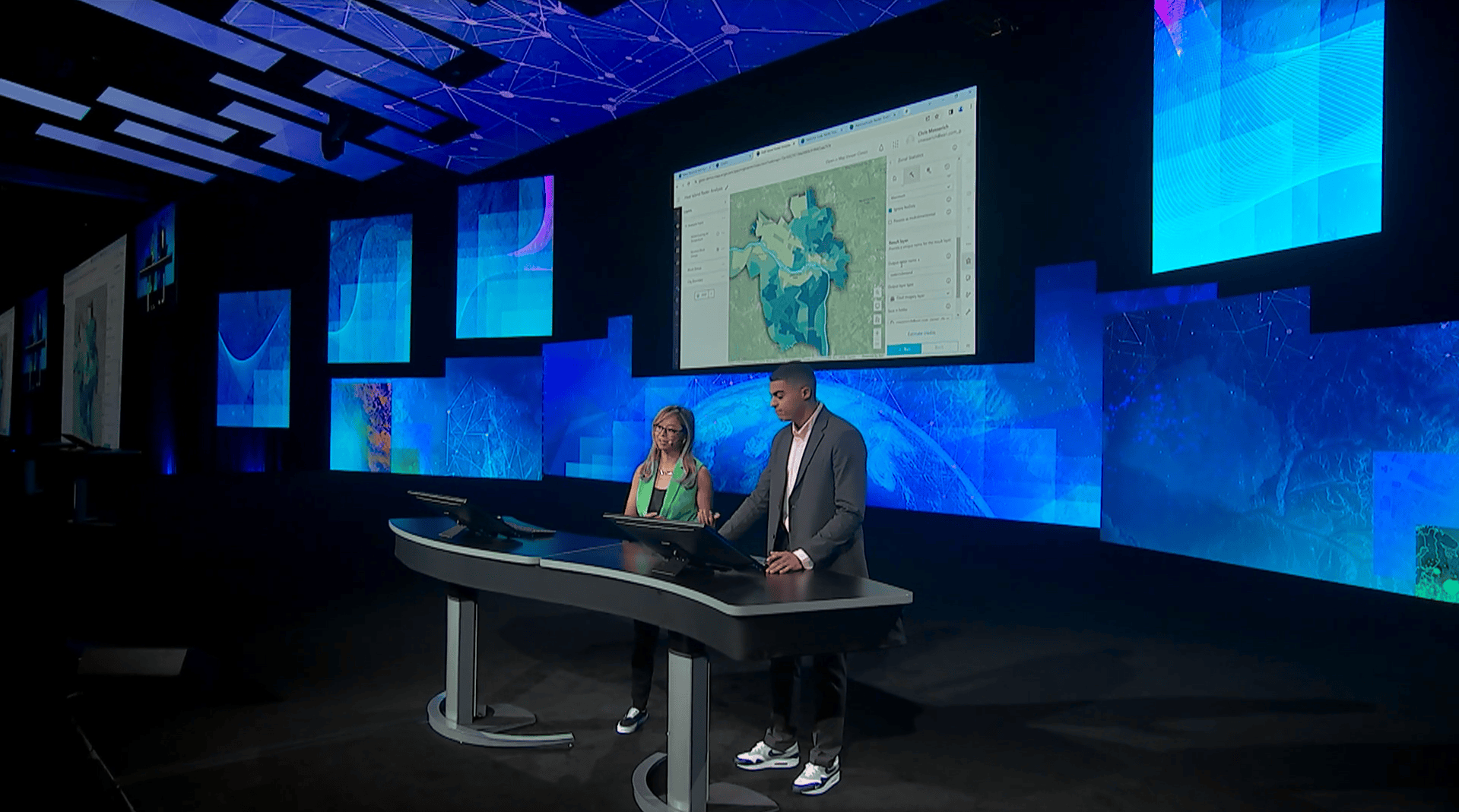Two presenters stand on a stage in front of a screen showing a map of urban heat islands in the city of Richmond, Virginia