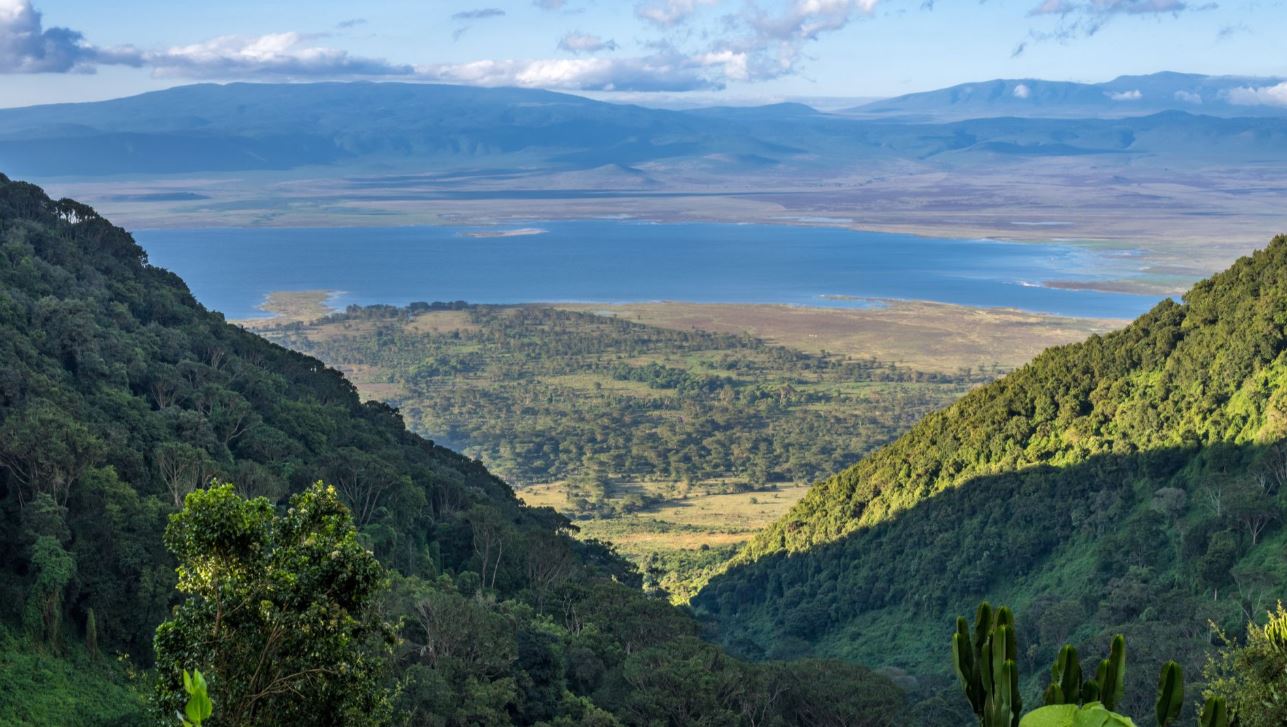 A landscape mountain view overlooking a green rangeland, lake, and mountains