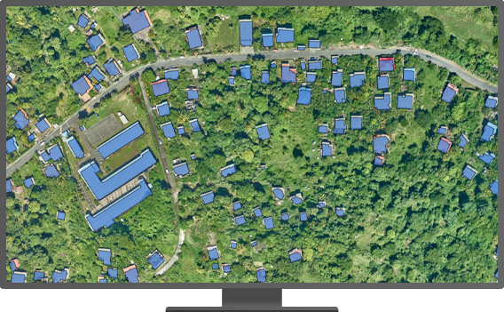 A desktop monitor displaying an aerial view of lush green land dotted with structures that are highlighted in periwinkle