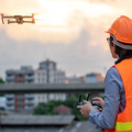 A person wearing an orange hard hat and safety vest looking at a hovering drone