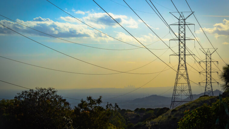 Utility transmission towers standing in a lush landscape under a blue sky 