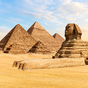 A grouping of Egyptian pyramids with the Sphinx in the foreground under a hazy pale blue sky
