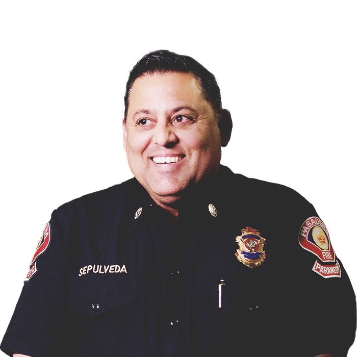 Oscar Sepúlveda, capitán de bomberos de la ciudad de Pasadena, vistiendo su uniforme y sonriendo, y un desfile de fondo