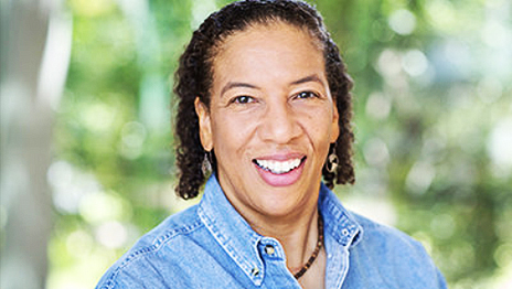 Dr. Dawn Wright smiling in a blue denim collared shirt with sun-dappled leaves in the background