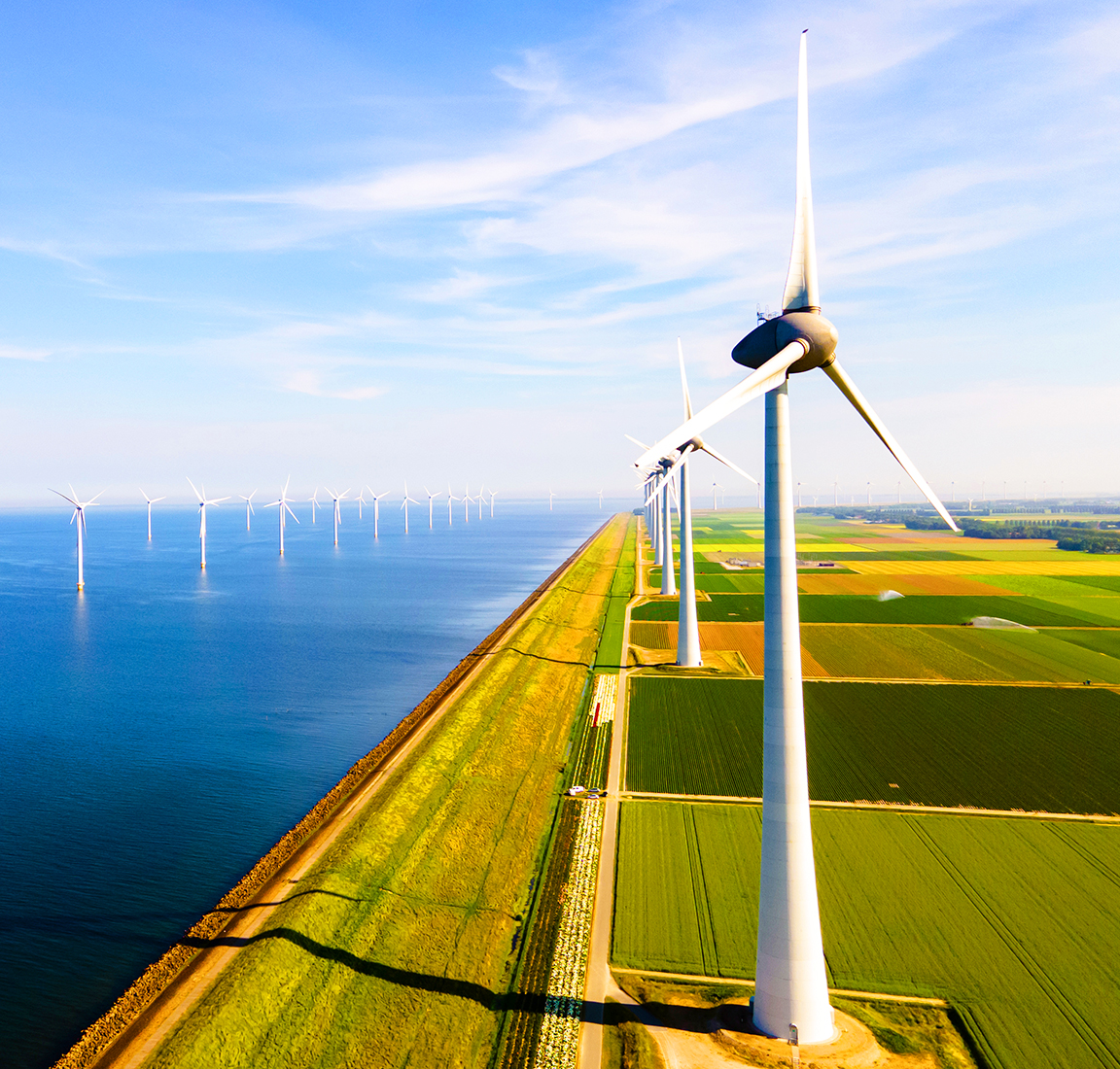 Aerial image of a green field beside a shoreline with wind turbines visible in the distance
