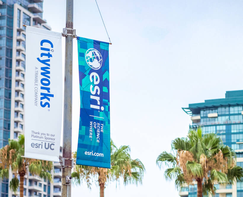 Signage for Esri UC hanging on a streetlight with a skyscraper in the background