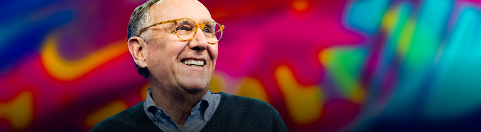 Jack Dangermond wearing a gray sweater and smiling with a colorful abstract background