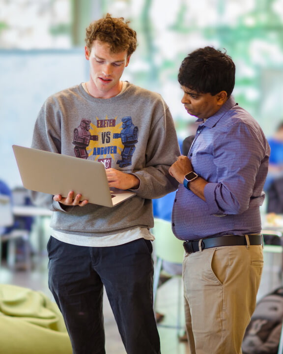 Two people in a modern sunlit classroom discussing a laptop display