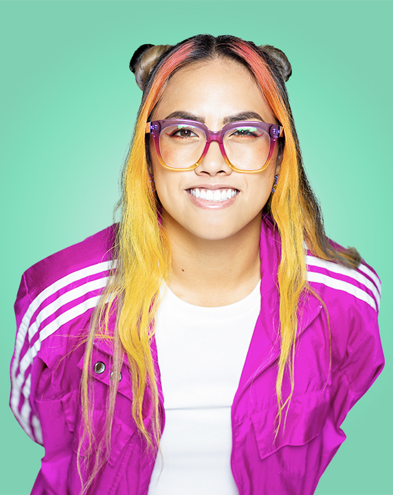 A person with pink and yellow hair, matching glasses, and a vivid pink jacket winking at the camera