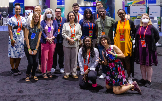A group of smiling people wearing red conference lanyards posing for a photo in a large expo area