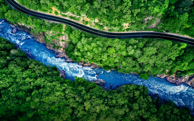 An aerial image of a winding blue river beside a road through a dense green forest
