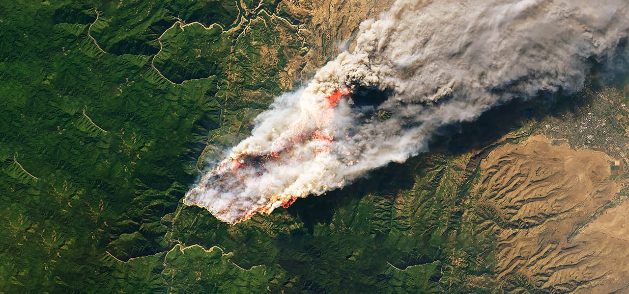 An aerial image of an active wildfire burning on the border of a forest and densely populated area.